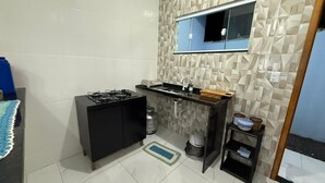 Una cocina compacta con estufa a gas, un fregadero, microondas y una pequeña alacena con utensilios de cocina.
