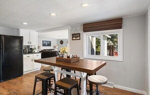 Une cuisine avec une table en bois, des tabourets, un réfrigérateur noir et une fenêtre donnant sur un beau paysage.