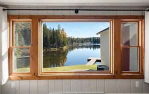 A room with a large window overlooking a lake, a wooden deck, and a small outdoor seating area. - Private Lakefront House, 15 feet to water, Kayaks, Game Room, Dog Friendly (Wolverine)