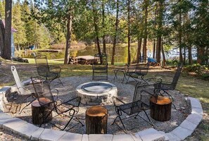 Un espace circulaire aménagé avec des chaises en métal et un foyer central, le tout entouré d’une bordure en pierre.