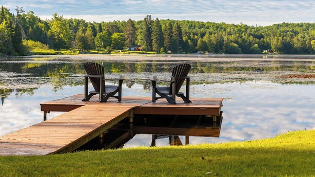 A wooden dock extending into a calm lake with two chairs facing the water, surrounded by lush greenery and trees. - Private Lakefront House, 15 feet to water, Kayaks, Game Room, Dog Friendly (Wolverine)