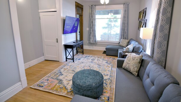 Una sala de estar con sofá, reposapiés y televisor sobre un mueble.