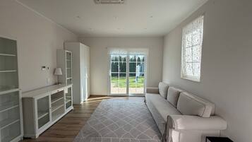 Ein modernes Zimmer mit einem weißen Sofa, einer Glastruhe, einem gemusterten Teppich und einer Schiebeglas-Tür, die zu einem Außenbereich führt.