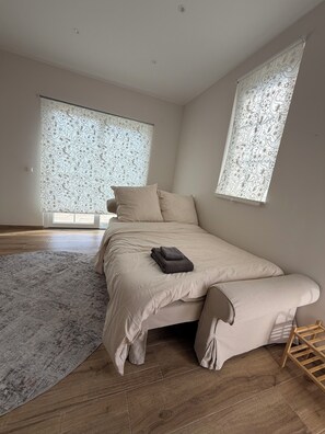 Ein Schlafzimmer mit Bett, Teppich und Fenster mit gemustertem Vorhang.