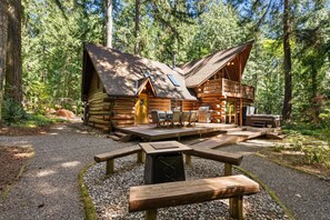 Eine Blockhütte mit einer Terrasse, Sitzgelegenheiten im Freien und einem Picknicktisch.