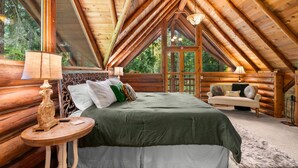 Un dormitorio tipo cabaña de madera con techo elevado, una cama con ropa de cama verde, una mesa redonda de madera y un sofá.