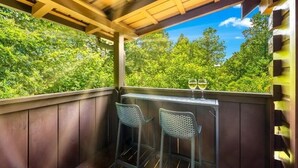 Un patio al aire libre con vigas de madera, dos sillas de metal y una mesa con una copa de vino.