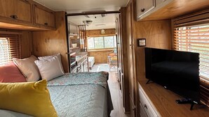 Interior compacto de una caravana con cama, kitchenette y televisor.