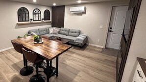 Een moderne woonkamer met een hoekbank, een houten eettafel met stoelen, en een inbouwkast met decoratieve objecten.