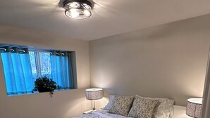 Een slaapkamer met een groot bed, twee nachtkastjes met lampen, een raam met gordijnen en een plafondlamp.