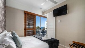 Quarto de hotel com cama, televisão na parede, varanda e vista, e um banco.