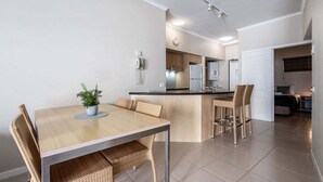 Cozinha moderna com ilha central, área de refeições com cadeiras de vime e um telefone visível na parede.