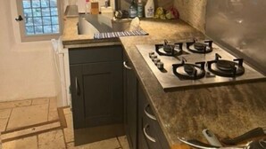 Een keuken met een gasfornuis, kastjes, een raam en een aanrecht met verschillende spullen.