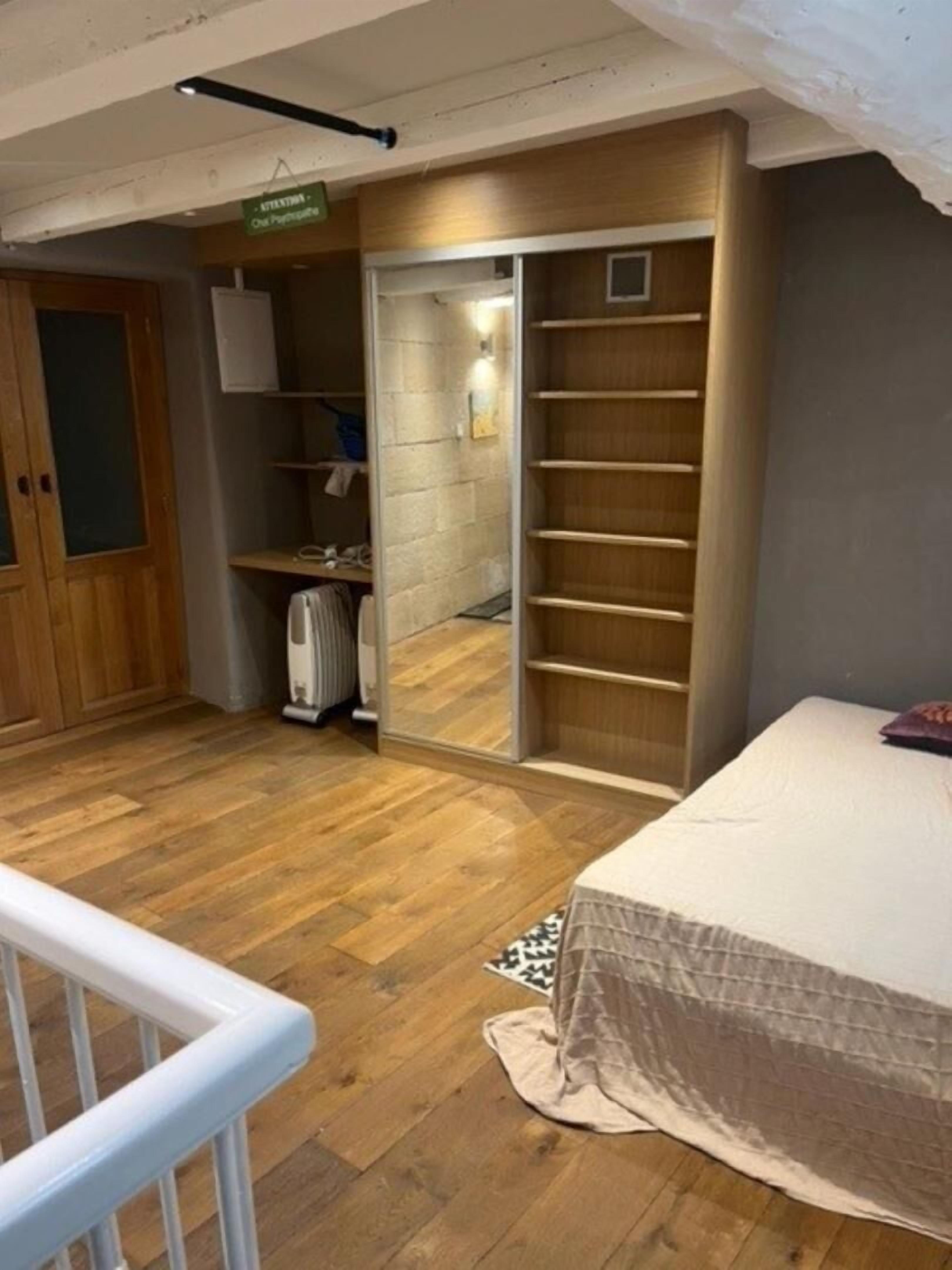 Une chambre à coucher comprenant un lit, un plancher en bois, une armoire, un radiateur et une étagère.