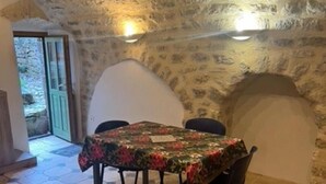 Een eethoek met een tafel bedekt met een bloemenkleed, vloertegels met een honingraatpatroon, stenen muren en een deur naar buiten.