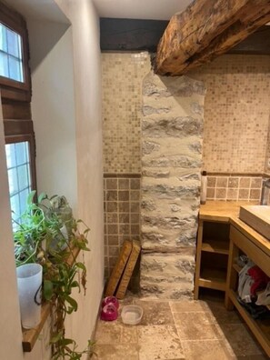 Une petite salle de bain rustique avec un mur en pierre, des poutres en bois et une étagère en bois sur laquelle est posée une plante.