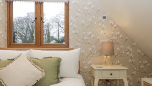 A bedroom with a bed, pillows, a nightstand, a lamp, and a window. - Charming apartment set in the Wye Valley, Herefordshire (Perrystone Hill, Ross-on-Wye)