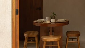 A dining area with a round wooden table, two wooden stools, and a door leading to another room. - Meridiano 48 Loft, One-Bedroom Accommodation (Mérida)