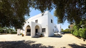 A white building with arched entrances, a gravel driveway, and parked cars. - Marubium - Scorcialupi (Maruggio)