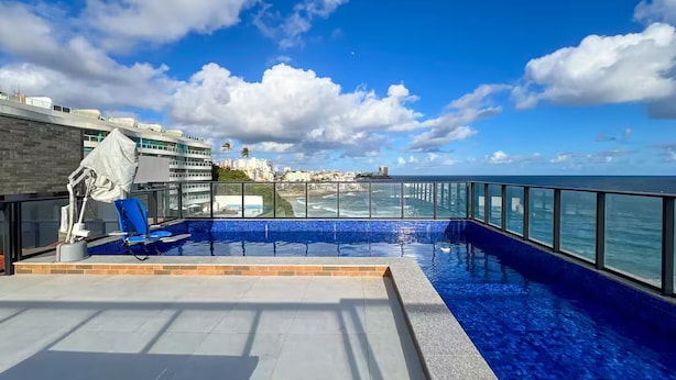 A rooftop infinity pool with a clear view of the ocean and city skyline. - Saint Bartz Residence - Ondina (Salvador)