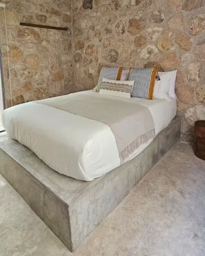 Ein Bett mit weißer Bettwäsche, einer Steinwand und einem Holzkopfende.