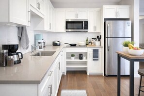 A modern kitchen with white cabinets, stainless steel appliances, a coffee maker, and a fruit bowl. - Steps to Greenway | Private, parking, sunny patio | 15 min to YVR, UBC, downtown (Vancouver)
