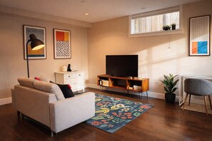 A living room with a sofa, TV stand, and a window with plants. - Steps to Greenway | Private, parking, sunny patio | 15 min to YVR, UBC, downtown (Vancouver)