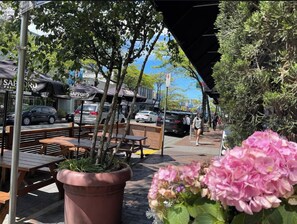 An outdoor seating area with wooden tables and benches, surrounded by potted plants and a street view. - Steps to Greenway | Private, parking, sunny patio | 15 min to YVR, UBC, downtown (Vancouver)