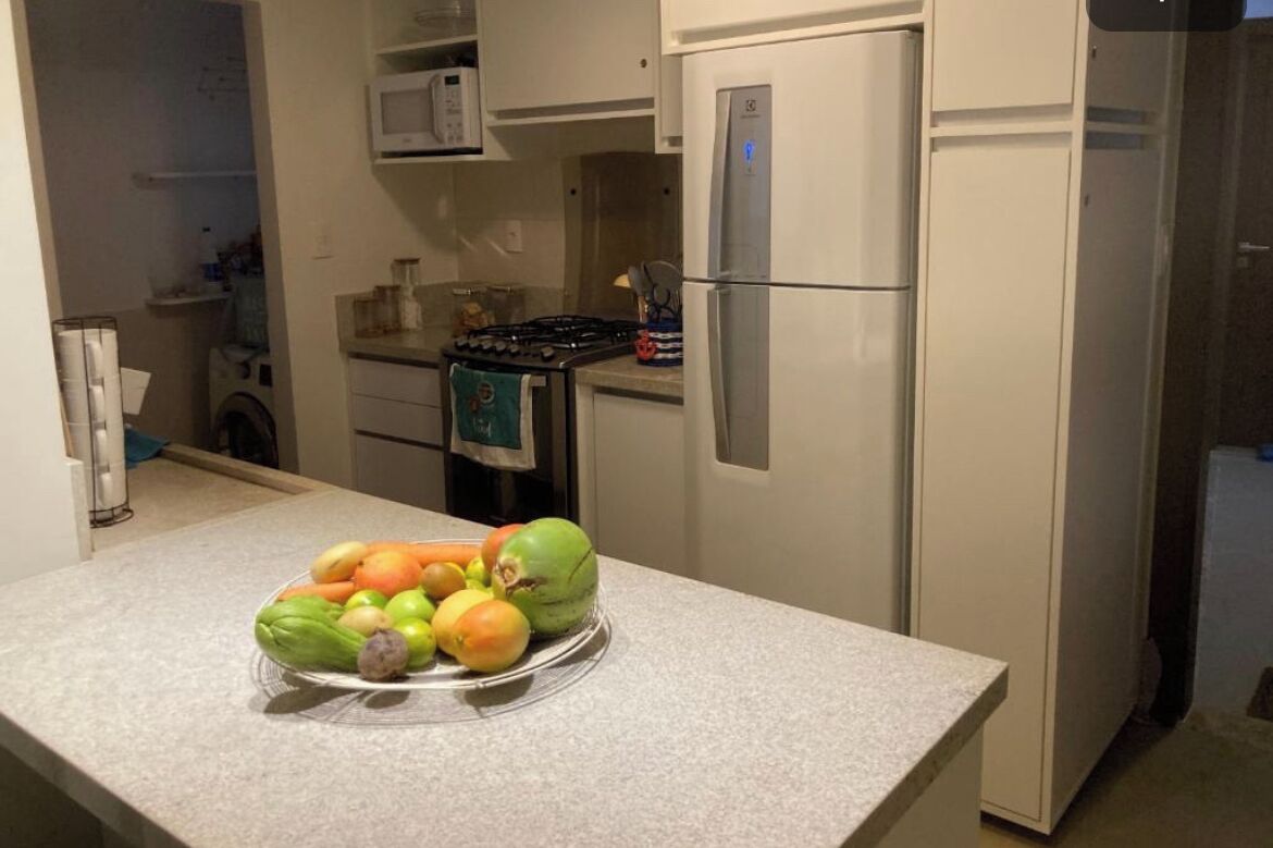A kitchen with a refrigerator, microwave, stove, and a bowl of fruit on the counter.