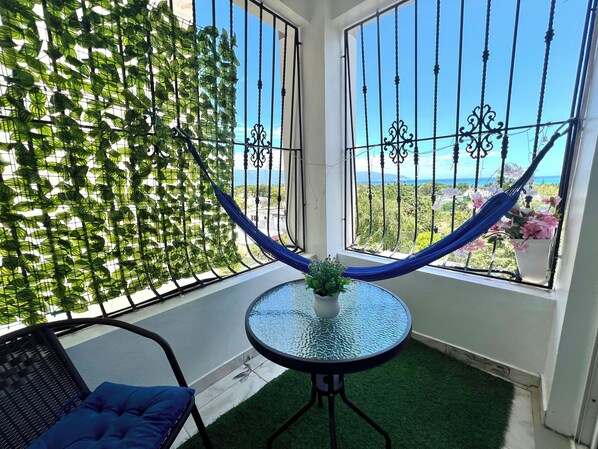 Un balcon avec vue, un hamac, une table avec une plante et une chaise.