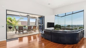 Ein modernes Wohnzimmer mit einer großen Eckcouch, einem Flachbildfernseher und einer Glastür, die auf eine Außenpatio mit Grill und Essbereich führt.