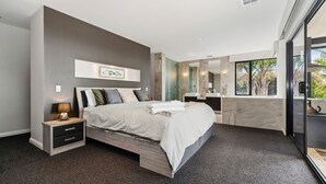 A modern bedroom with a large bed, bedside tables, a mirror, and a view of the outdoors. - The Ultimate Family Entertainer. Bay Views, Spa & Games (Mount Martha)