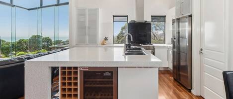 Een moderne keuken met een groot keukeneiland, roestvrijstalen apparatuur en een wijnkoeler.
