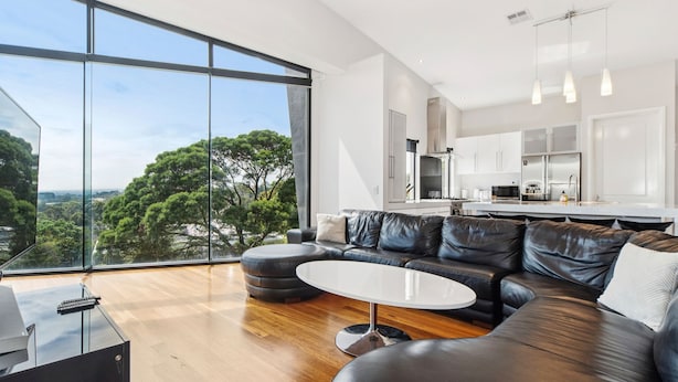 A modern living room with a leather sofa, a round coffee table, and a large window offering a view of trees and buildings. - The Ultimate Family Entertainer. Bay Views, Spa & Games (Mount Martha)