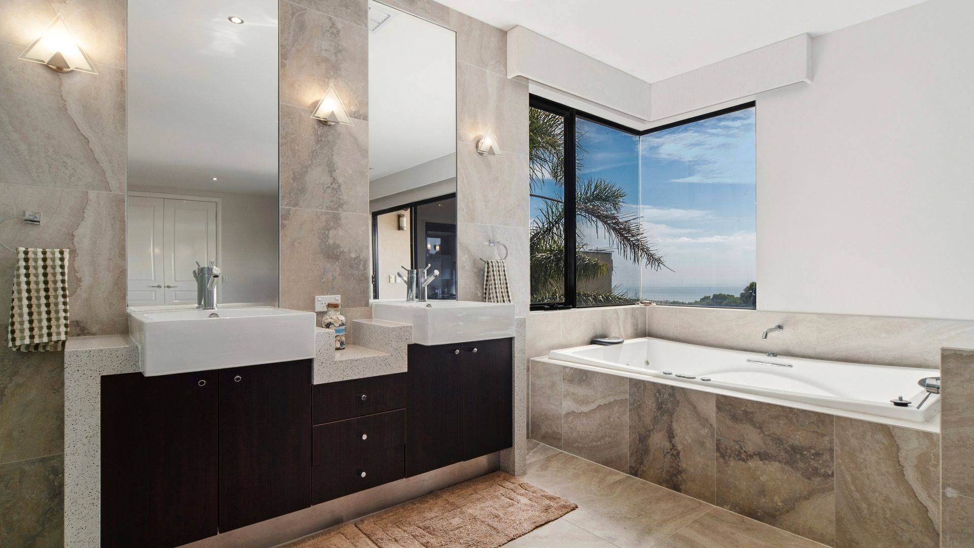 Ein modernes Badezimmer mit einem großen Spiegel, zwei Waschbecken, einer Badewanne und Meerblick.