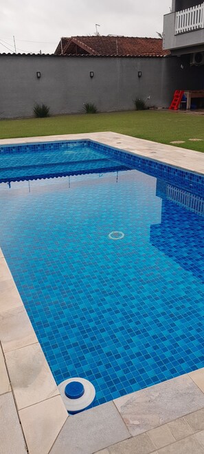 Une piscine aux carreaux bleus, une clôture blanche et une échelle rouge.