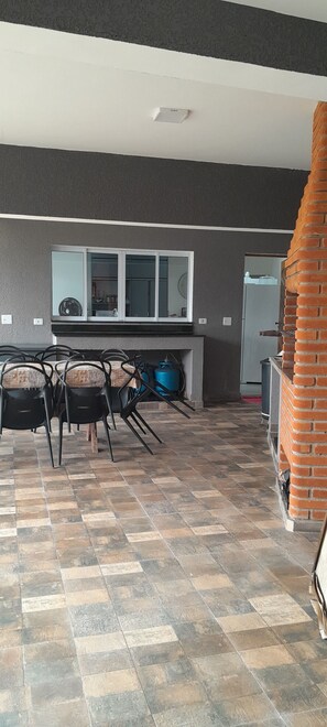 Une pièce dotée d’un sol carrelé, d’une table à manger avec des chaises, d’un coin cuisine avec des placards et d’une cheminée en briques.