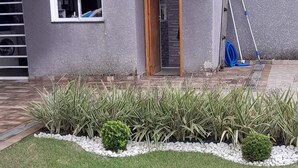 A residential house with a grey exterior, a wooden door, a window, and a small garden with stepping stones. - House with a large and cozy pool, with space for the whole family, 100m from the beach. (Itanhaém)