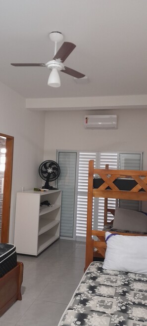 Une chambre avec un lit superposé, un bureau avec un ventilateur, un ventilateur de plafond et un appareil de climatisation.