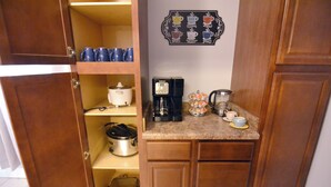 Une cuisine compacte équipée d’une machine à café, d’une bouilloire et d’un présentoir pour tasses à café.