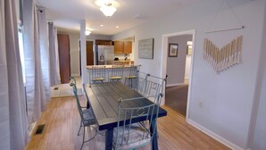 Une salle à manger avec une table en bois et des chaises en métal, une cuisine en arrière-plan et un élément décoratif fixé au mur.