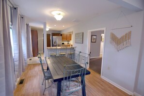 A dining room with a wooden table and metal chairs, a kitchen in the background, and a wall-mounted decorative piece.