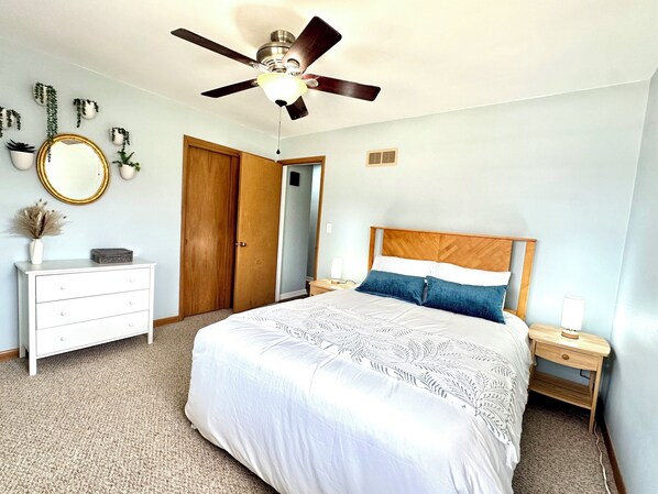 Un dormitorio con cama, mesita de noche, cómoda, ventilador de techo y una puerta.