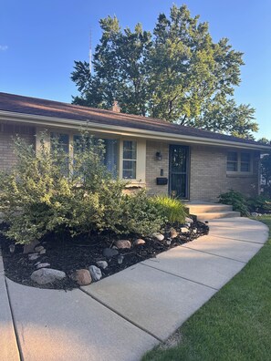A single-story house with a brick facade, a front porch, and a well-maintained garden with shrubs and rocks. - 3BR Rockford Getaway w/ Game Room-Prime Location Near Everything (Rockford)
