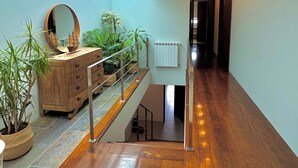 Un intérieur spacieux agrémenté d’un escalier en bois, d’un grand miroir et de plantes en pot.