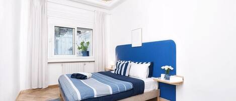 A bedroom with a bed, a window, a bedside table, and a hanging light fixture.