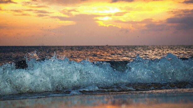 Tramonto sull'oceano con le onde che si infrangono sulla spiaggia.