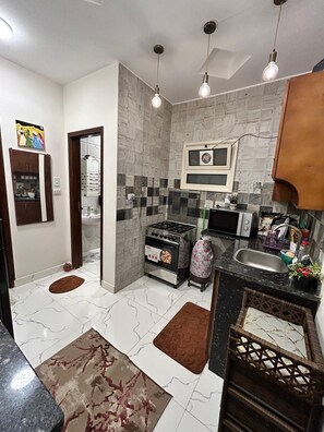 A kitchen with a gas stove, microwave, sink, and a tiled backsplash. - Cozy 1-bedroom apartment in peaceful Red Sea Governorate with AC (Red Sea Governorate)