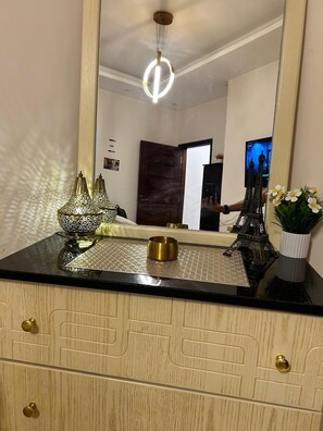 A room with a wooden cabinet, a mirror reflecting a door, a small Eiffel Tower model, and a vase with flowers on the counter. - Cozy 1-bedroom apartment in peaceful Red Sea Governorate with AC (Red Sea Governorate)