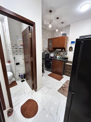 A modern kitchen with a refrigerator, wooden cabinets, a microwave, and a washing machine. - Cozy 1-bedroom apartment in peaceful Red Sea Governorate with AC (Red Sea Governorate)